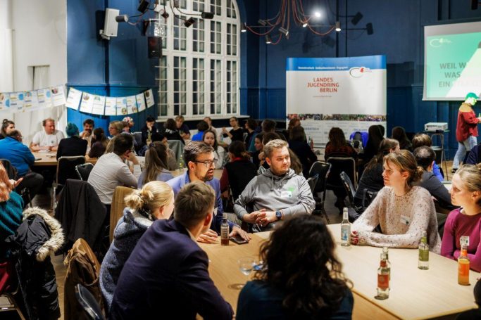 Gruppen von Menschen diskutieren in einem hell erleuchteten Raum bei einer Veranstaltung des Landesjugendring Berlin.