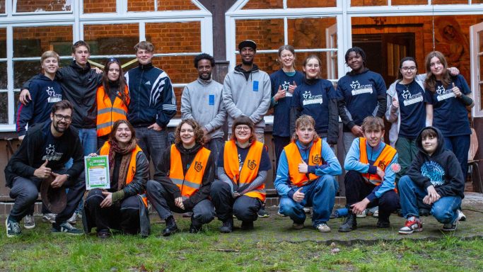 Gruppe von Jugendlichen in Warnwesten, die fröhlich vor einem Gebäude posieren.