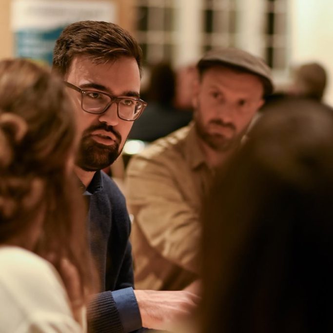 Männliche Teilnehmer in einem Gespräch bei einer Diskussion, in einem gemütlichen Raum.