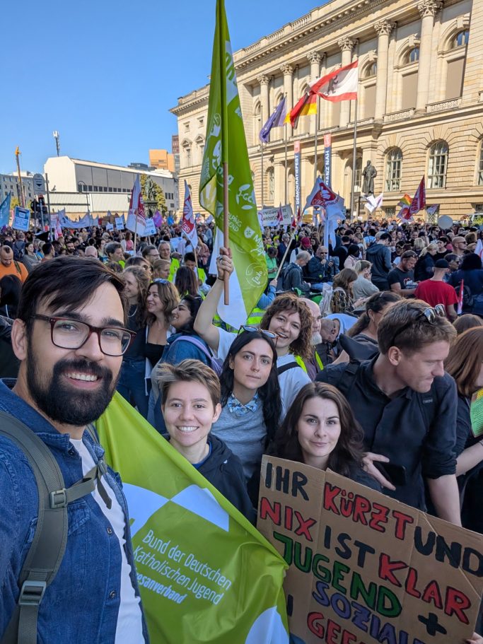 Felix posiert vor einer Menschenmenge mit Protestschildern und Fahnen.