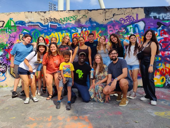 Gruppenfoto von Menschen vor einer bunten Graffiti-Wand, alle lächeln.